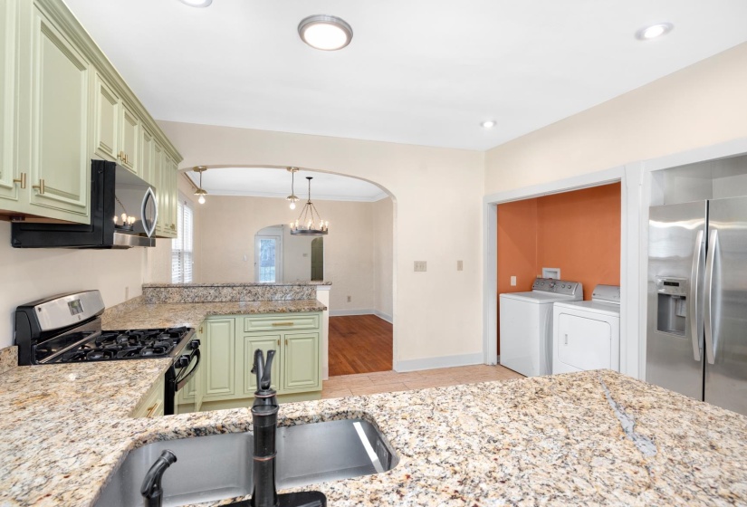 Kitchen with stainless steel appliances, washing machine and dryer, light stone counters, and green cabinetry