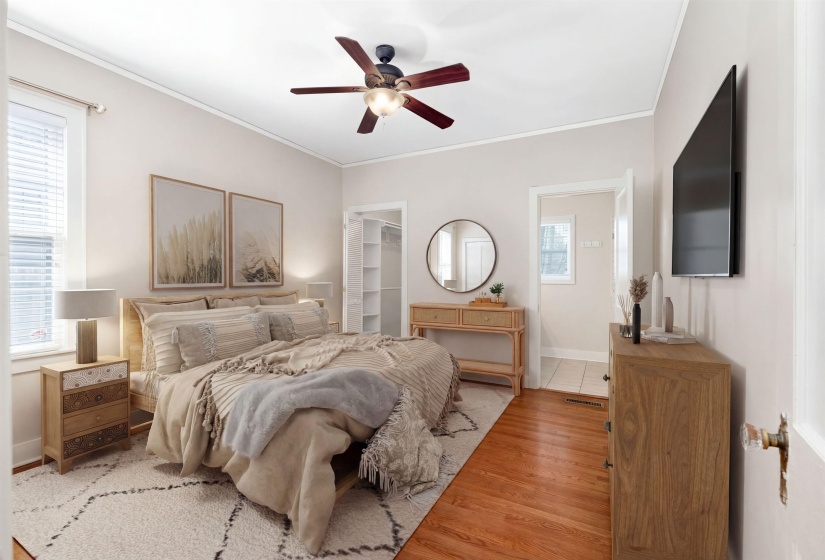 Bedroom featuring a walk in closet, wood finished floors, a ceiling fan, and ornamental molding