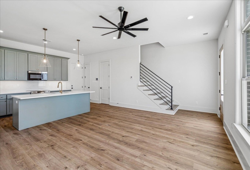 Kitchen featuring gray cabinets, pendant lighting, a ceiling fan, a kitchen island with sink, and stainless steel microwave