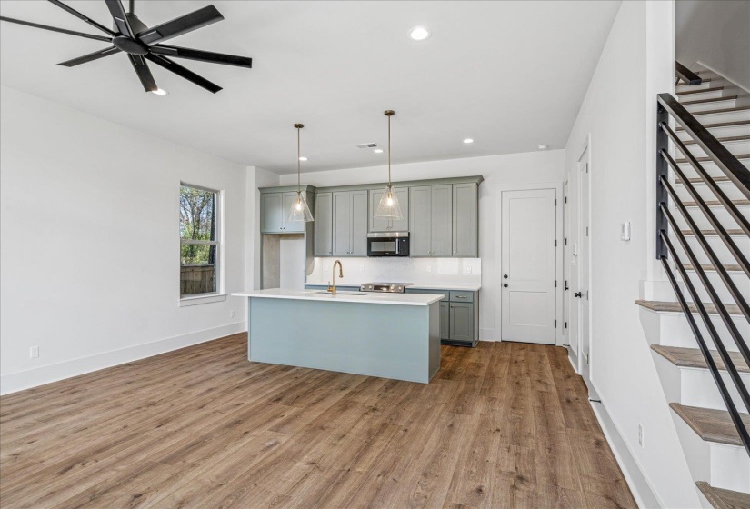 Kitchen with gray cabinetry, pendant lighting, dark wood-type flooring, stainless steel microwave, and a center island with sink