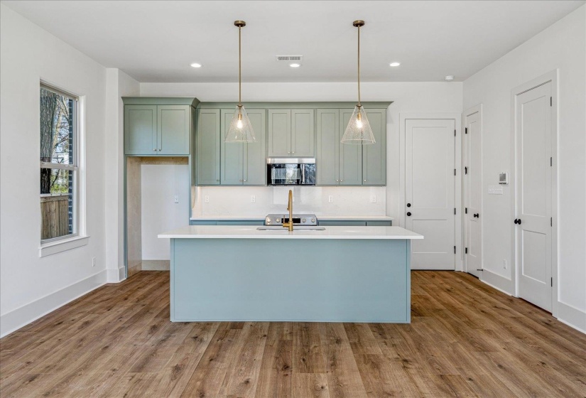 Kitchen featuring a kitchen island with sink, stainless steel microwave, light wood finished floors, and pendant lighting