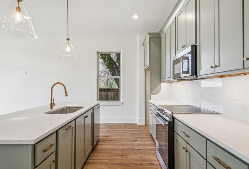 Kitchen with stainless steel appliances, light stone countertops, gray cabinetry, a center island with sink, and light wood-type flooring