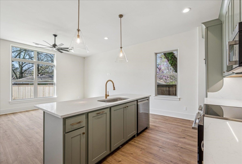 Kitchen with an island with sink, stainless steel appliances, light stone counters, hanging light fixtures, and light wood finished floors