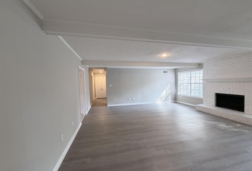 Spacious living area featuring wood-finish flooring, a white brick fireplace with hearth, and multiple large windows