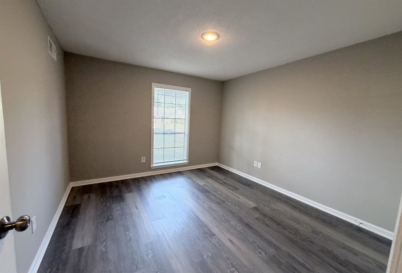 Interior room featuring wood-finish flooring, a white-framed window, neutral-toned walls, recessed ceiling lighting, and white baseboards