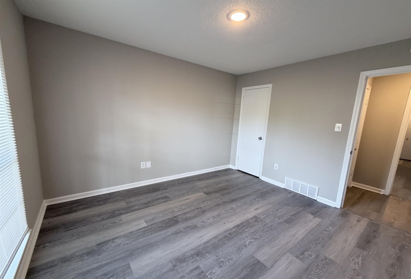 Interior room featuring wood-finish flooring, light grey painted walls, white baseboards, a white door with a round knob, and a ceiling-mounted recessed light fixture