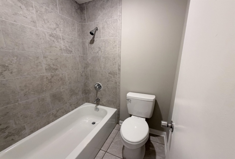 Bathroom featuring a white bathtub, gray rectangular wall tiles, chrome fixtures, and a white toilet