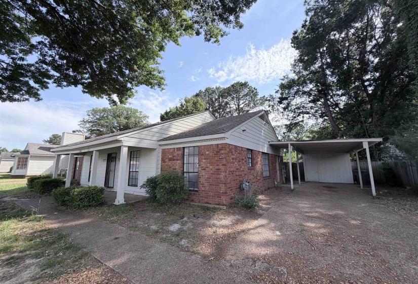 Brick and siding exterior featuring a covered front porch, carport, and mature trees