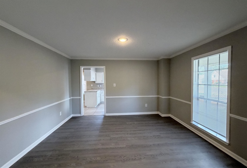 Spacious room featuring wood-finish flooring, two-tone wall paint, white crown molding, and a large window with blinds