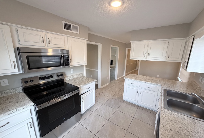Modern kitchen featuring white cabinetry, granite-finish countertops, stainless steel appliances, and tile flooring