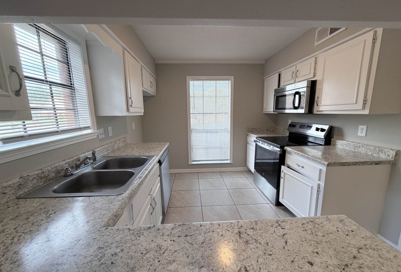 Kitchen featuring white cabinetry, light-toned countertops, stainless steel appliances, and tile flooring