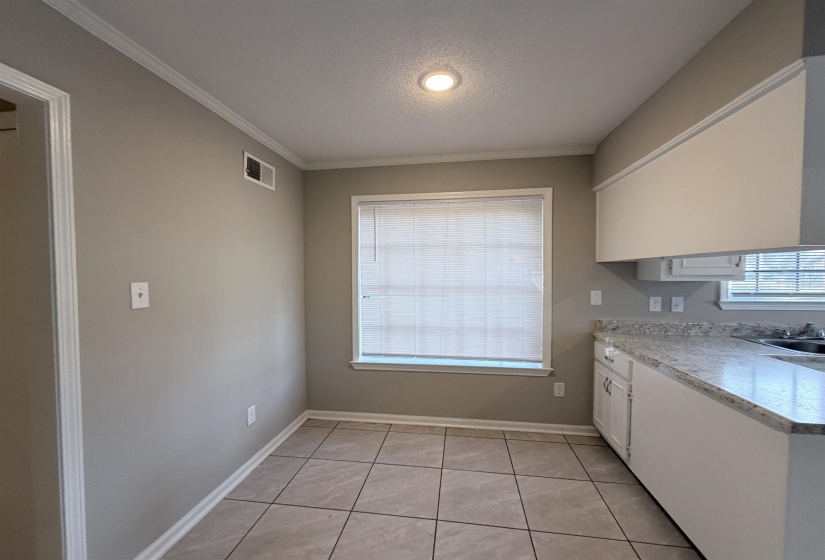 Kitchen area featuring light-toned tile flooring, light gray wall paint, white crown molding, and recessed lighting