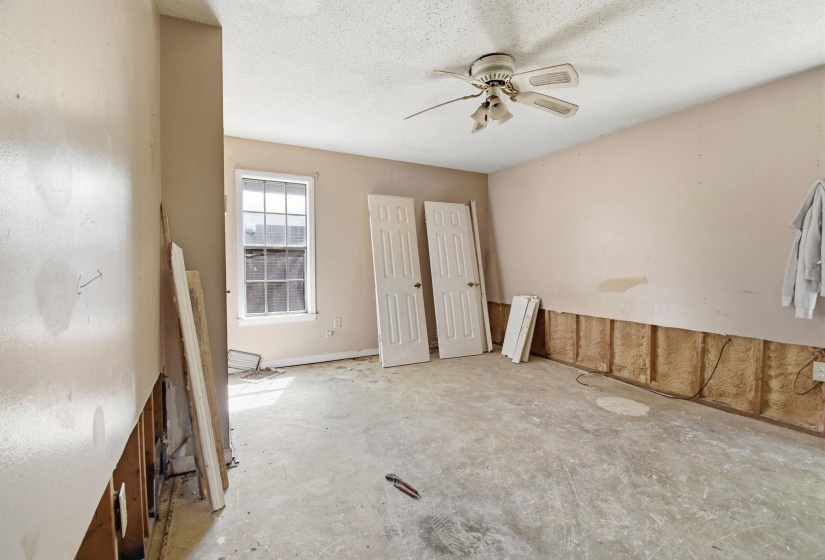 Room featuring a ceiling fan, a window with gridded panes, two white paneled doors, and exposed wall framing