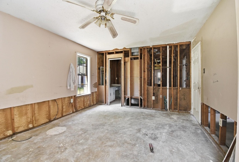 Interior space with exposed wall studs, a single window, a ceiling fan, and a solid white door