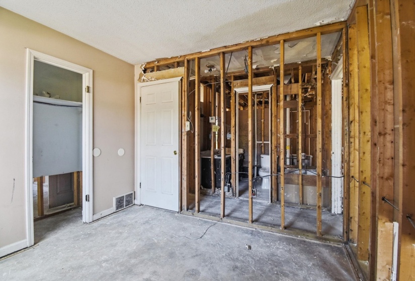 Interior room featuring exposed wall studs, concrete subflooring, and a paneled white door