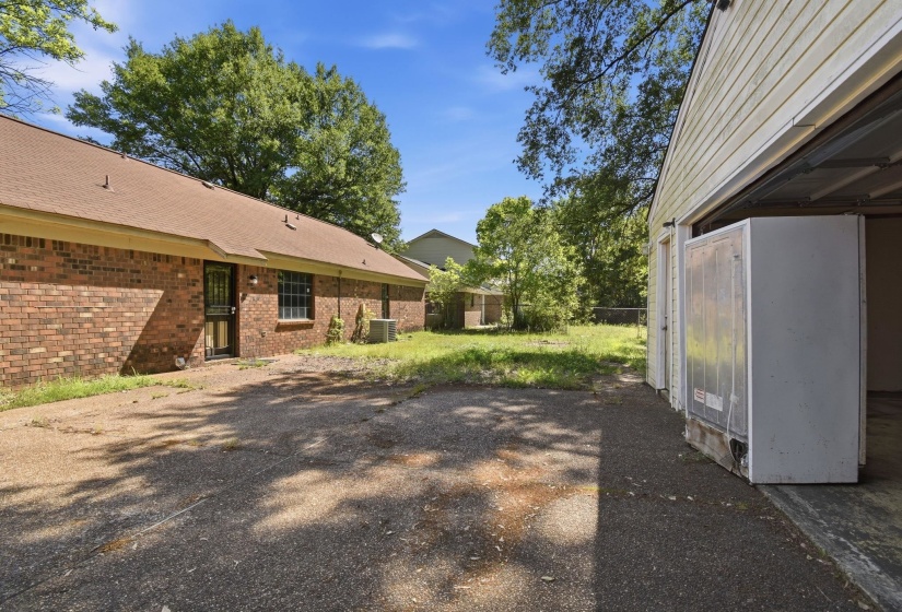 Attached garage with a white paneled exterior, a spacious paved driveway, and a brick-sided structure with multiple windows and a rear entry door