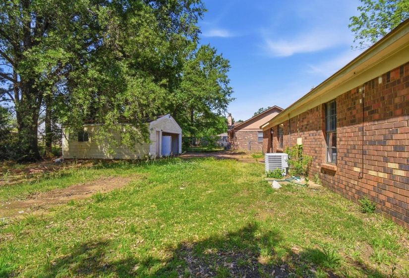Expansive rear yard featuring a detached storage shed with a roll-up door, mature trees, and a brick exterior on the main residence