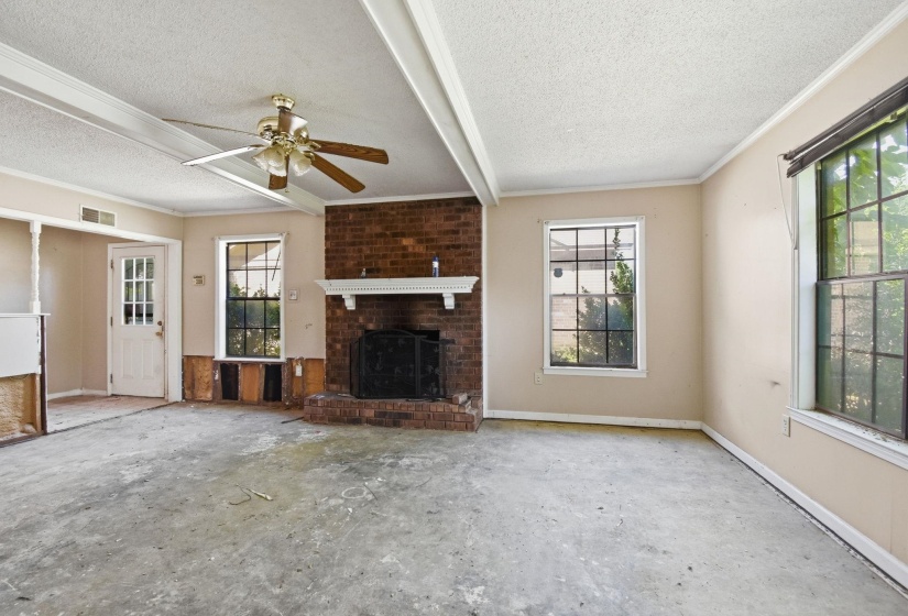 Spacious room featuring a brick fireplace with a white mantel, multiple windows, exposed ceiling beams, and a ceiling fan