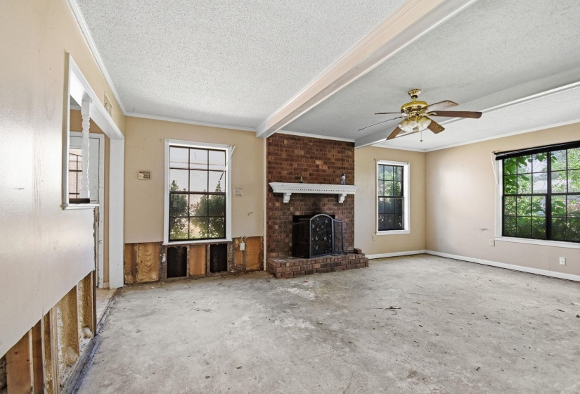 Spacious interior featuring a brick fireplace with a white mantel, multiple windows, a ceiling fan, and crown molding details