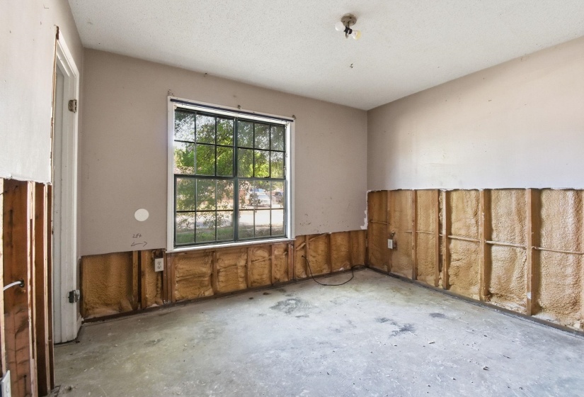 Interior room featuring a large window, exposed wall studs, and a concrete floor