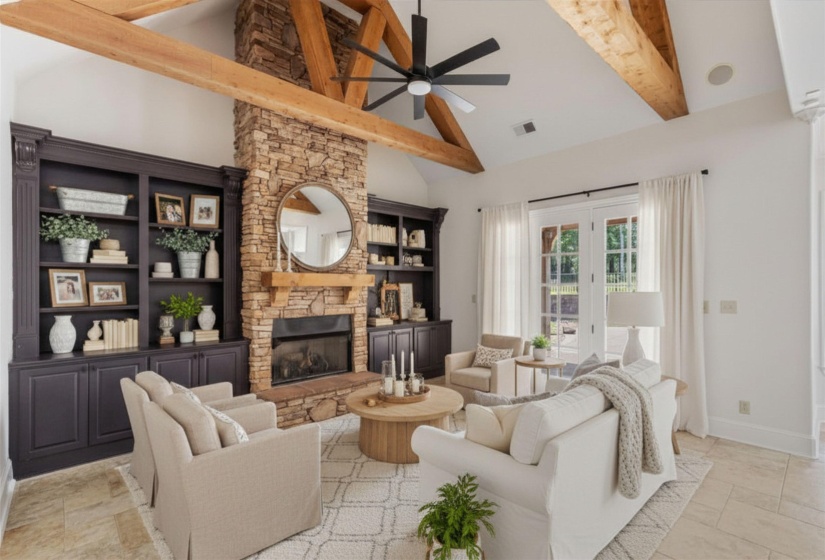 Kitchen opens seamlessly to the Hearth Room featuring a floor-to-ceiling stone fireplace, exposed beams, and built-ins—perfect for gathering and everyday living. Virtually staged photo.