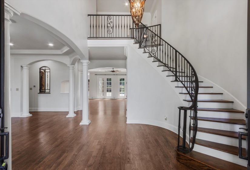 Entrance Foyer opens to soaring two-story ceilings with sweeping curved staircase, iron balusters, hardwood floors, and arched openings leading to spacious Living Areas filled with natural light.