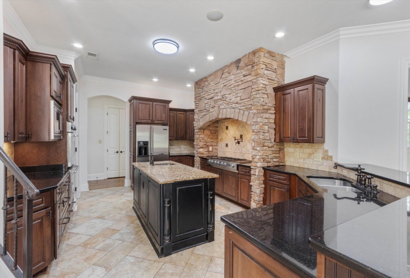 Impressive chef’s Kitchen with stone-surround gas range, tile backsplash, pot filler, and granite island with prep sink. Opens to the Hearth Room with floor-to-ceiling stone fireplace, exposed beams, and built-ins—perfect for everyday living.