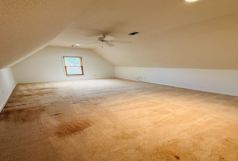 Spacious room with angled ceilings, a single window, and a ceiling fan