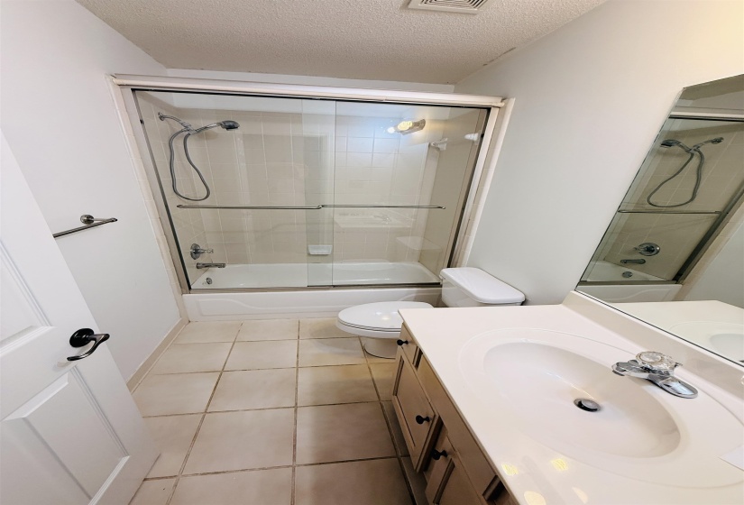 Bathroom featuring a vanity with an integrated sink, a sliding glass shower door, a white bathtub, and tile flooring
