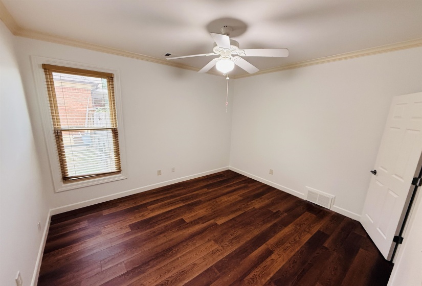 Room featuring wood-finish flooring, white walls, crown molding, and a ceiling fan with integrated lighting