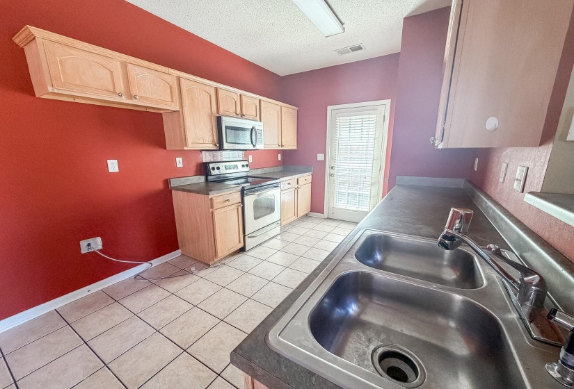 Kitchen featuring stainless steel appliances, light wood cabinetry, a double basin sink, and tile flooring