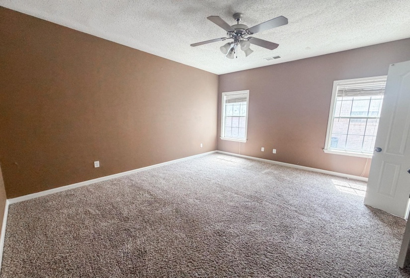 Spacious room featuring neutral-toned carpet, a ceiling fan with integrated lighting, and two windows with blinds