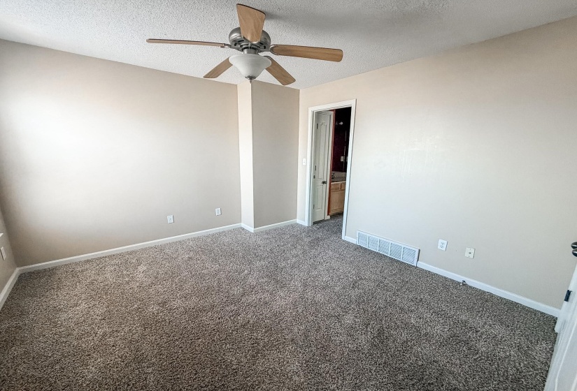 Spacious room featuring neutral-toned walls, textured carpet, and a ceiling fan with light fixture