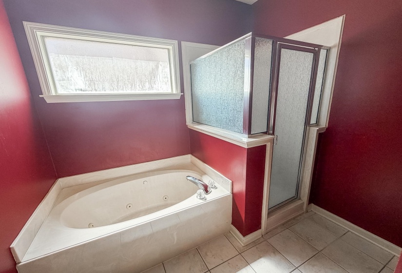 Soaking tub with tile surround, framed window, and adjacent glass-enclosed shower