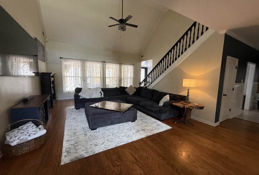 Spacious living area featuring high vaulted ceilings, warm wood-finish flooring, and a contemporary ceiling fan
