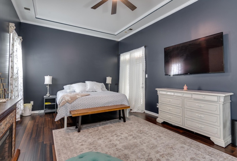 Spacious room featuring dark wood-finish flooring, a tray ceiling with crown molding, and a built-in fireplace with a stone surround