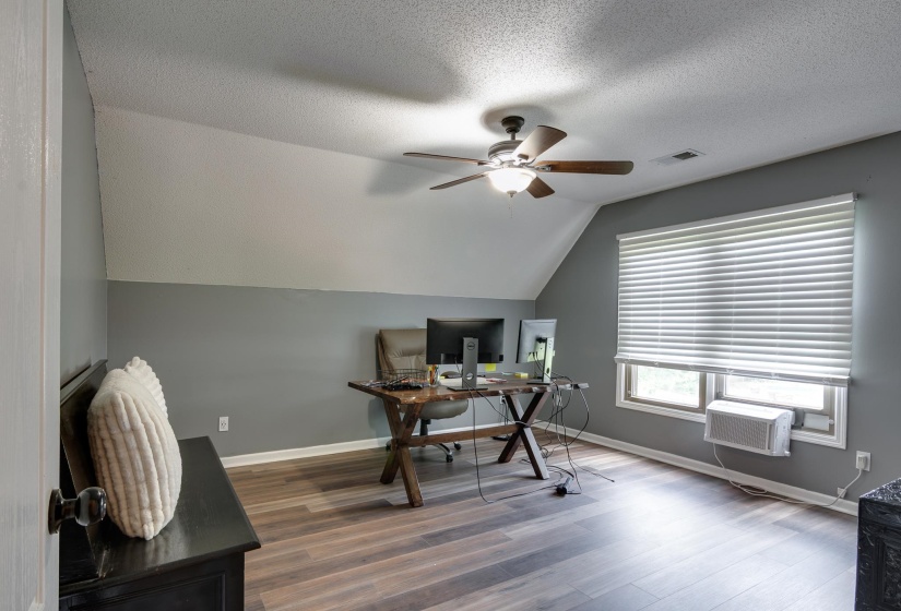 Attic room featuring sloped ceilings, wood-finish flooring, and a ceiling fan with integrated lighting