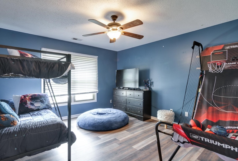 Spacious room featuring wood-finish flooring, a ceiling fan with integrated lighting, and a window with horizontal blinds