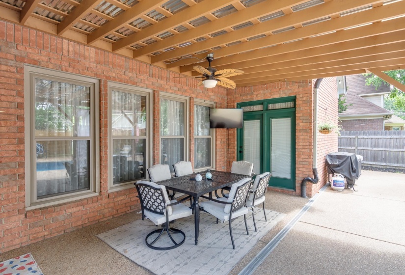 Covered patio featuring a wood-beam ceiling, exposed brick exterior, and a ceiling fan