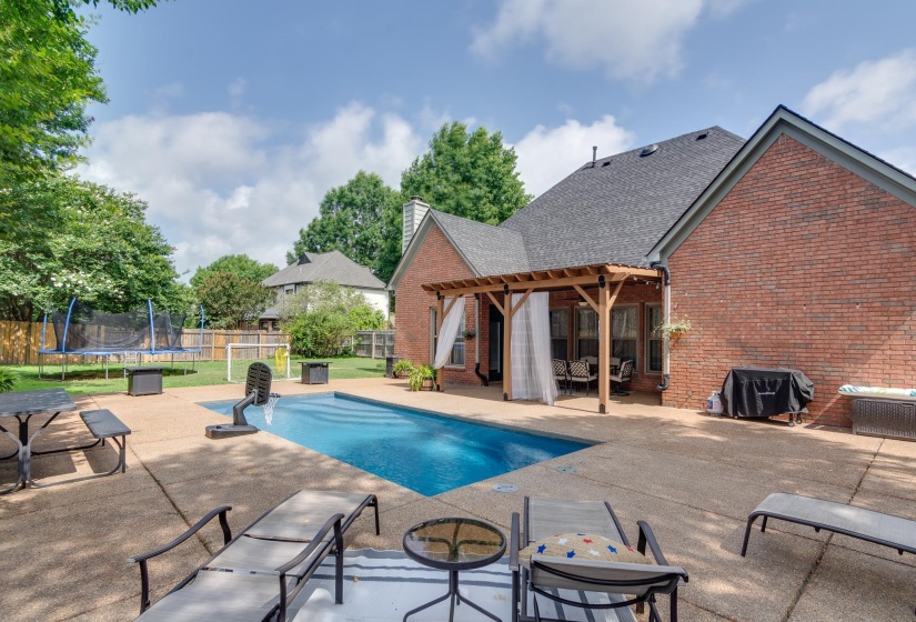 Expansive backyard featuring a rectangular in-ground swimming pool, a concrete patio, and a wood pergola with privacy drapes