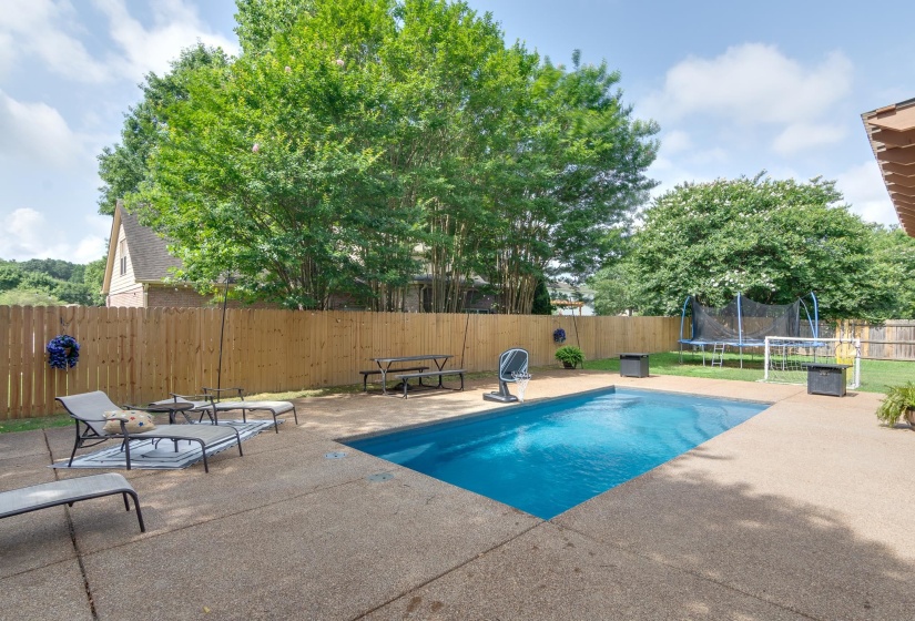Expansive backyard featuring a rectangular in-ground pool with a surrounding concrete patio, a wooden privacy fence, and mature trees providing natural screening