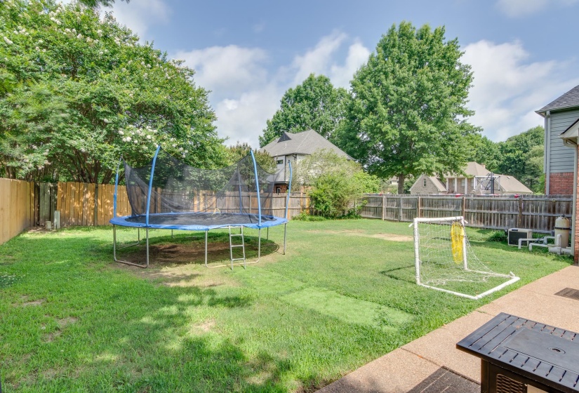 Expansive backyard featuring a privacy fence, mature trees, and a concrete patio
