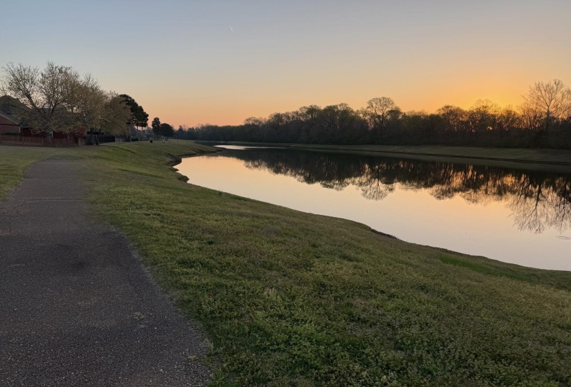 Waterfront setting with reflective surface, bordered by a paved pathway and grassy embankment