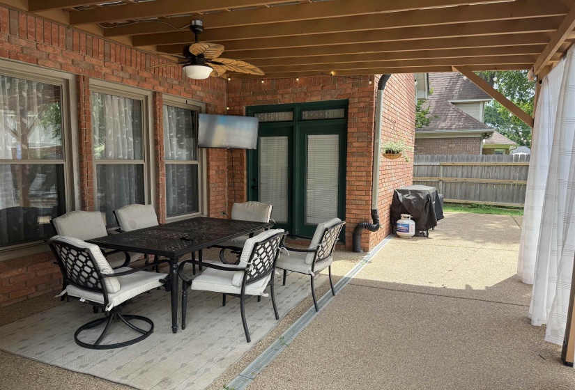 Covered patio featuring brick exterior, exposed beam ceiling, ceiling fan, and decorative string lighting