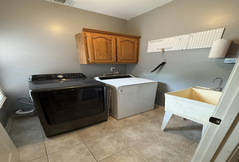 Dedicated laundry area featuring ceramic tile flooring, wood cabinetry, a utility sink, and ample wall space