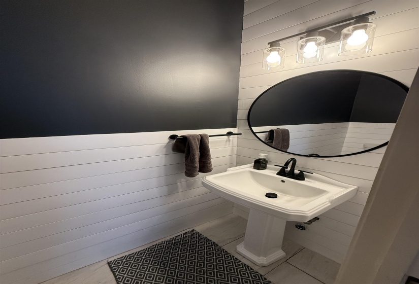 Pedestal sink with matte black faucet, set against white shiplap walls with a dark accent wall