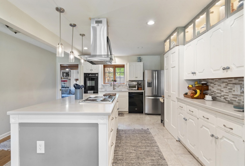 Kitchen featuring a large island with a cooktop, white cabinetry, stainless steel appliances, a mosaic tile backsplash, and recessed and pendant lighting