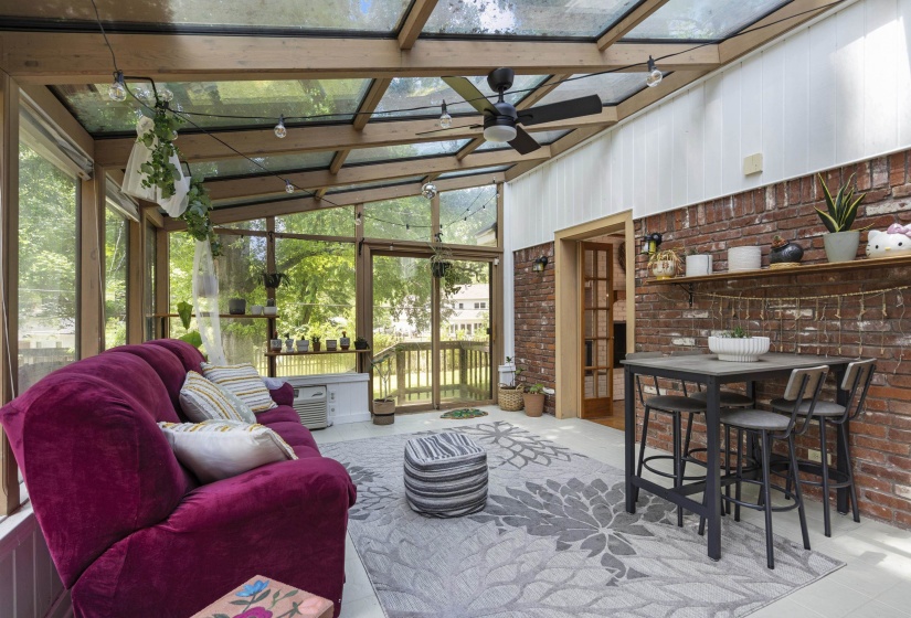 Light-filled sunroom featuring a glass roof, exposed wood beams, brick accent wall, and a ceiling fan