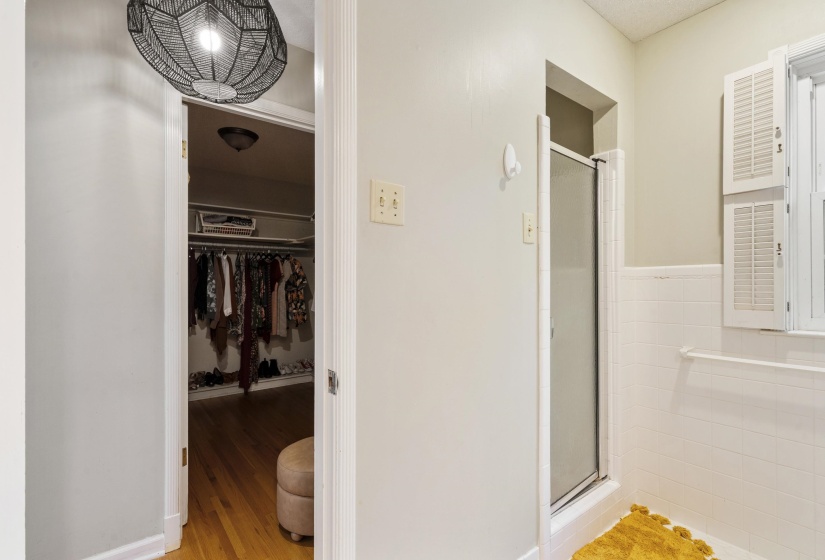 Bathroom featuring a glass-enclosed shower, white tile surround, and white louvered window shutters