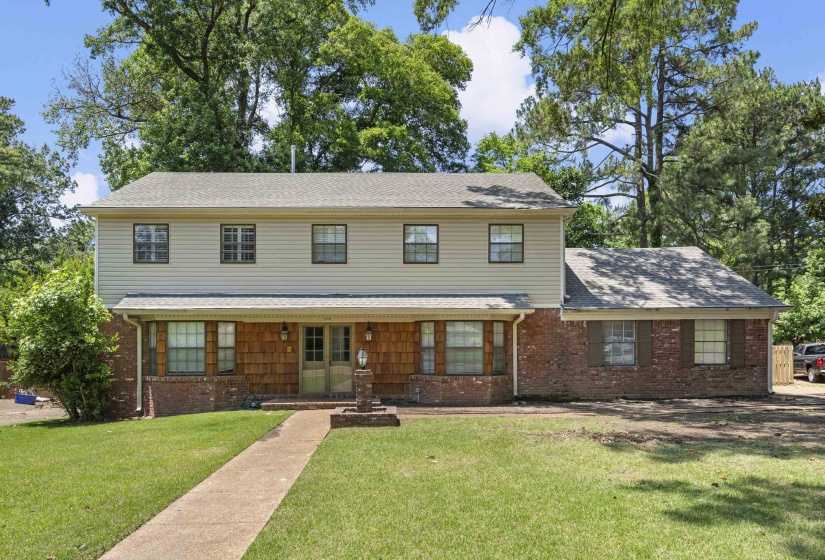 Two-story residence featuring a brick and siding exterior, a covered front porch, and mature trees